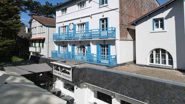 Un edificio de dos pisos con un balcón, un cartel que indica que es un hotel y restaurante, y un cielo azul despejado al fondo.