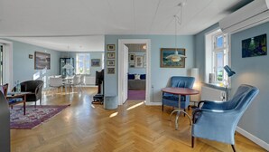 A spacious living area with a wooden floor, a dining table, and blue chairs. There is a television and a bookshelf in the room. - 5 bedroom awesome home in Erslev (Erslev)