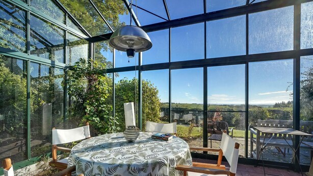 A conservatory with a round table and chairs, large windows, and a hanging light fixture. - 5 bedroom awesome home in Erslev (Erslev)
