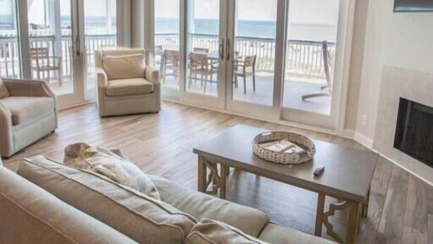 Un salón espacioso con ventilador de techo, chimenea y un amplio ventanal corredero que da a un balcón con vista al océano.