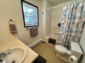 A bathroom with a sink, toilet, shower, and window.