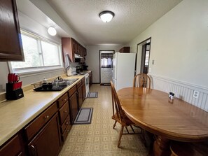 A kitchen with wooden cabinets, a countertop, a stove, a refrigerator, and a dining table with chairs.