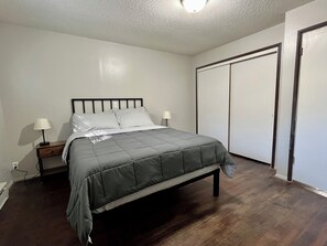 A bedroom with a bed, two bedside tables, a nightstand, a wardrobe, and a ceiling light.