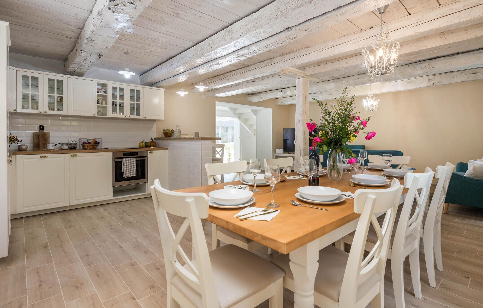 Un coin repas avec une table en bois dressée pour quatre personnes, des chaises blanches et un lustre.