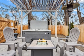 A patio with a fire pit, two Adirondack chairs, and a covered seating area with a pergola.