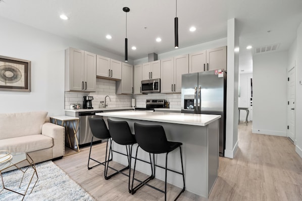 A modern kitchen with white cabinets, a central island with bar stools, stainless steel appliances, and pendant lighting.