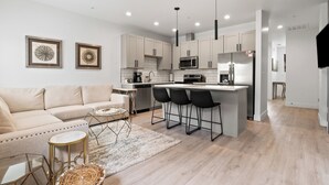 A modern kitchen with white cabinets, a central island with bar stools, a sofa, and a coffee table. - The *Minimalist's Escape* near Greenbelt & Winery with HOT TUB! (Garden City)