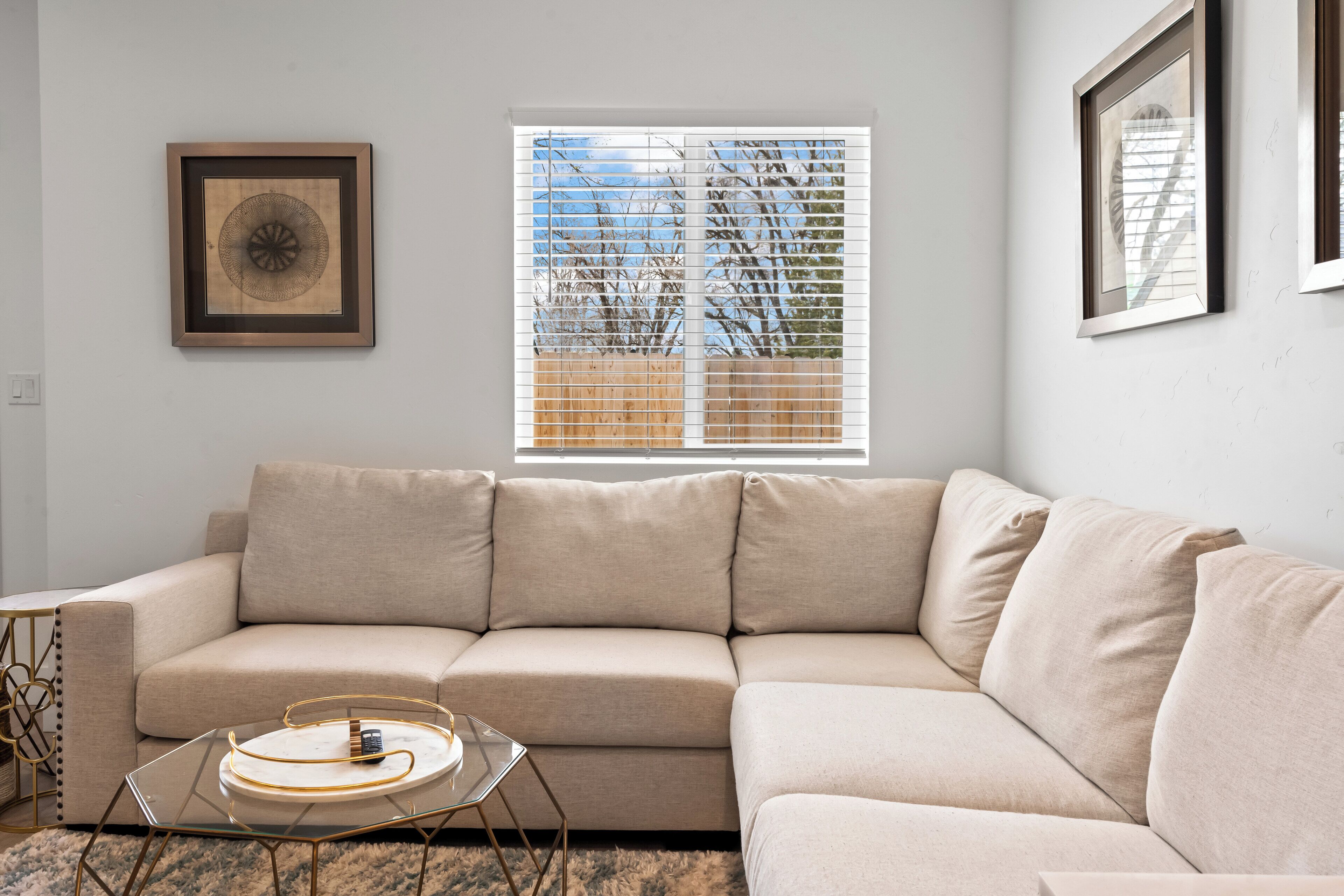 A living room with a beige sofa, a glass coffee table, and a framed artwork on the wall.