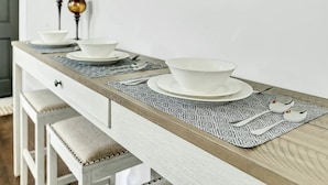 Una mesa de comedor con platos, tazones y cubiertos blancos, junto con dos copas de vino.