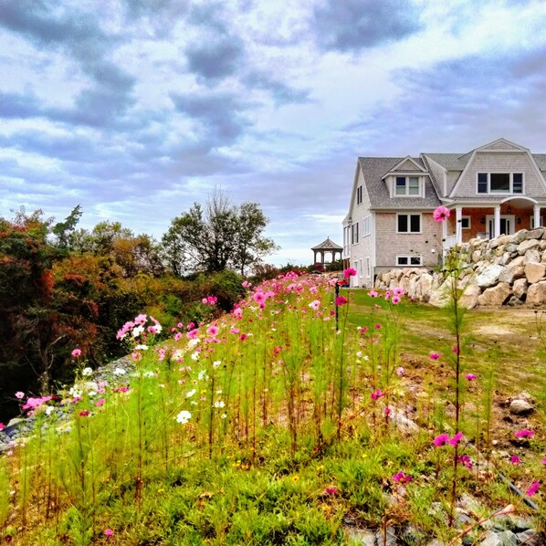 A house with a stone retaining wall and a garden with pink flowers. - Private Beach.  Fabulous Bay Views. WIFI (Brewster)
