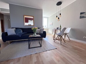 A modern living room with a dark blue sofa, a coffee table, and a dining area with a white table and chairs.