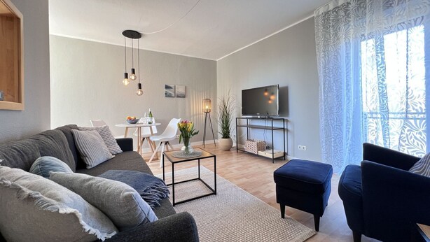 A modern living room with a sofa, ottoman, and TV stand. - Fewo Strandgut - "Strandgut" ... close to the beach and cozy! (Dahme)