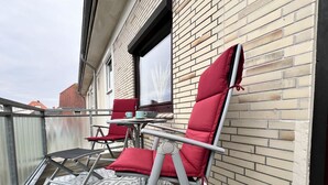 A balcony with two red chairs and a small table, a patterned rug, and a brick wall. - Fewo Strandgut - "Strandgut" ... close to the beach and cozy! (Dahme)