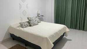 Una cama bien hecha con edredón blanco, dos almohadas estampadas y una lámpara de noche en una mesita.