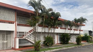 Un edificio de varios pisos con ventanas protegidas por barrotes, una escalera y palmeras en la parte delantera.