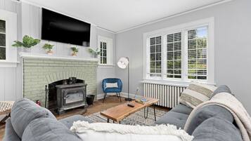 Ein Wohnzimmer mit Kamin, einer Couch, einem Sessel und einem an der Wand befestigten Fernseher.