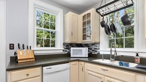 A kitchen with white cabinets, a microwave, a dishwasher, and hanging pots. - The Hawksbill Haus (w/ hot tub) (Waynesboro)
