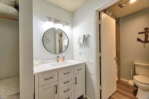 Ein Badezimmer mit weißem Waschtisch, einem runden Spiegel und einer Toilette.