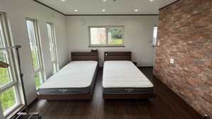 A modern hotel room with two single beds, large windows, a brick accent wall, and a view of the outside.