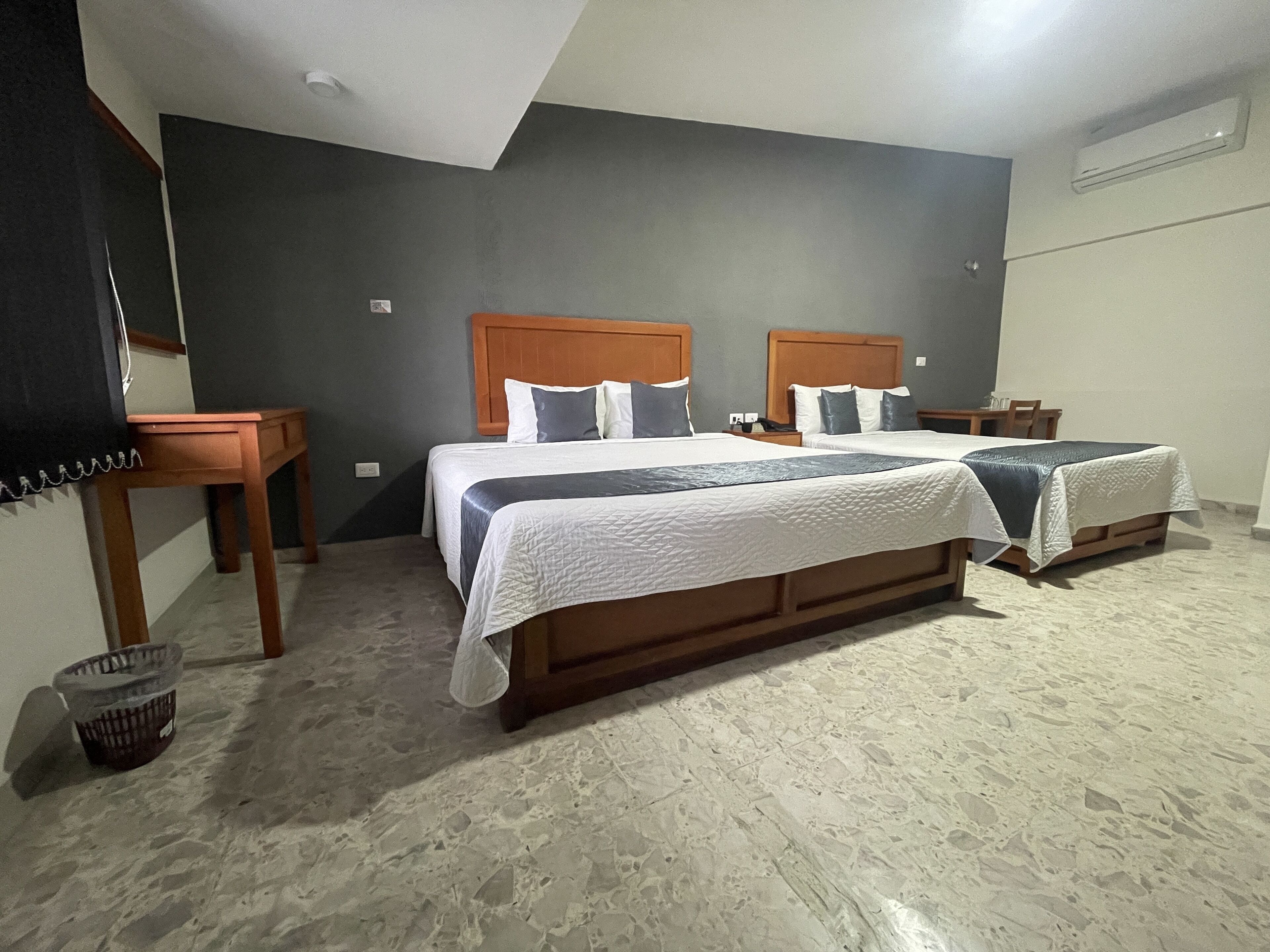 A hotel room with two beds, a wooden nightstand, a small table, and a trash bin.