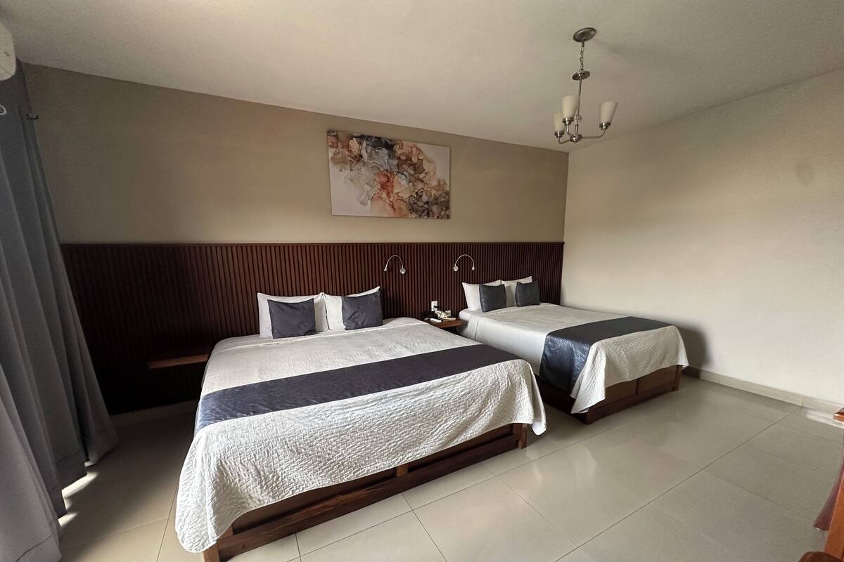 A hotel room with two beds, a wooden headboard, a painting on the wall, and a chandelier.