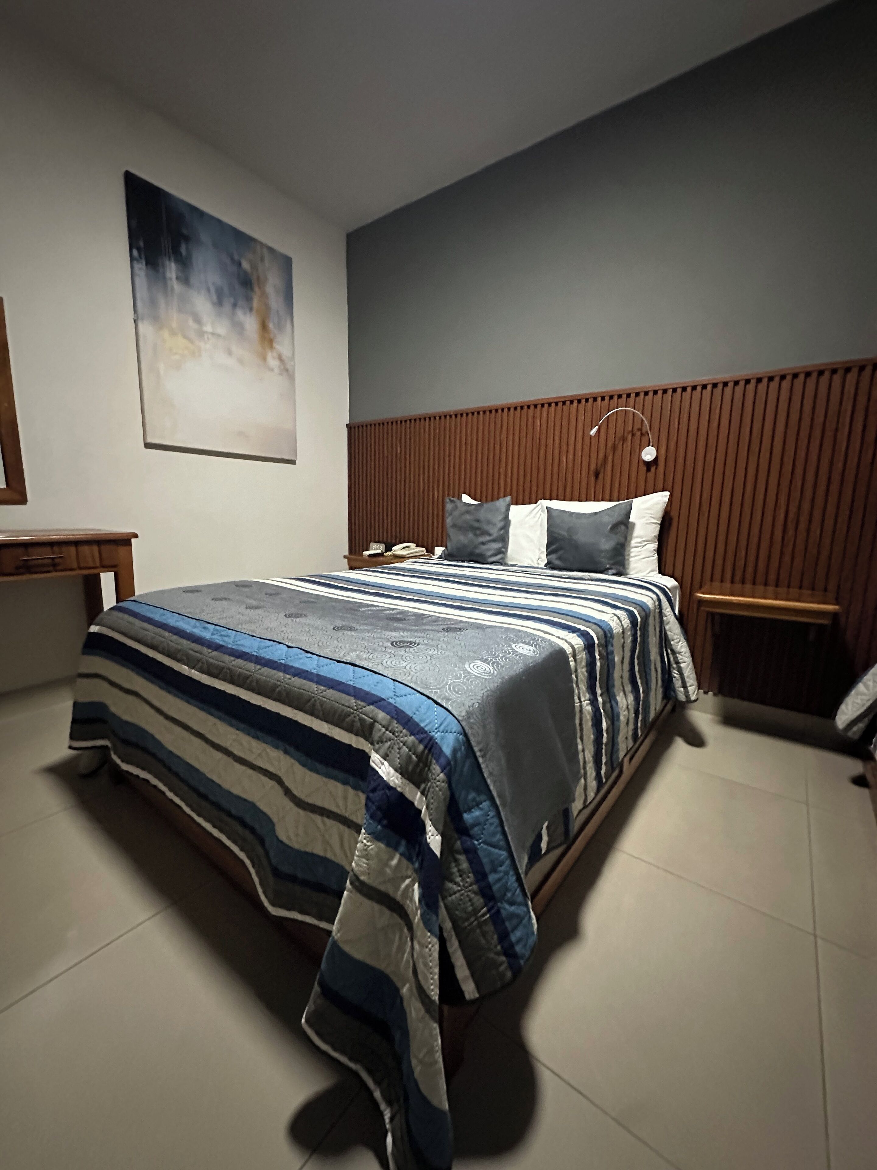 A modern bedroom with a large bed, wooden headboard, and a bedside table with a lamp.