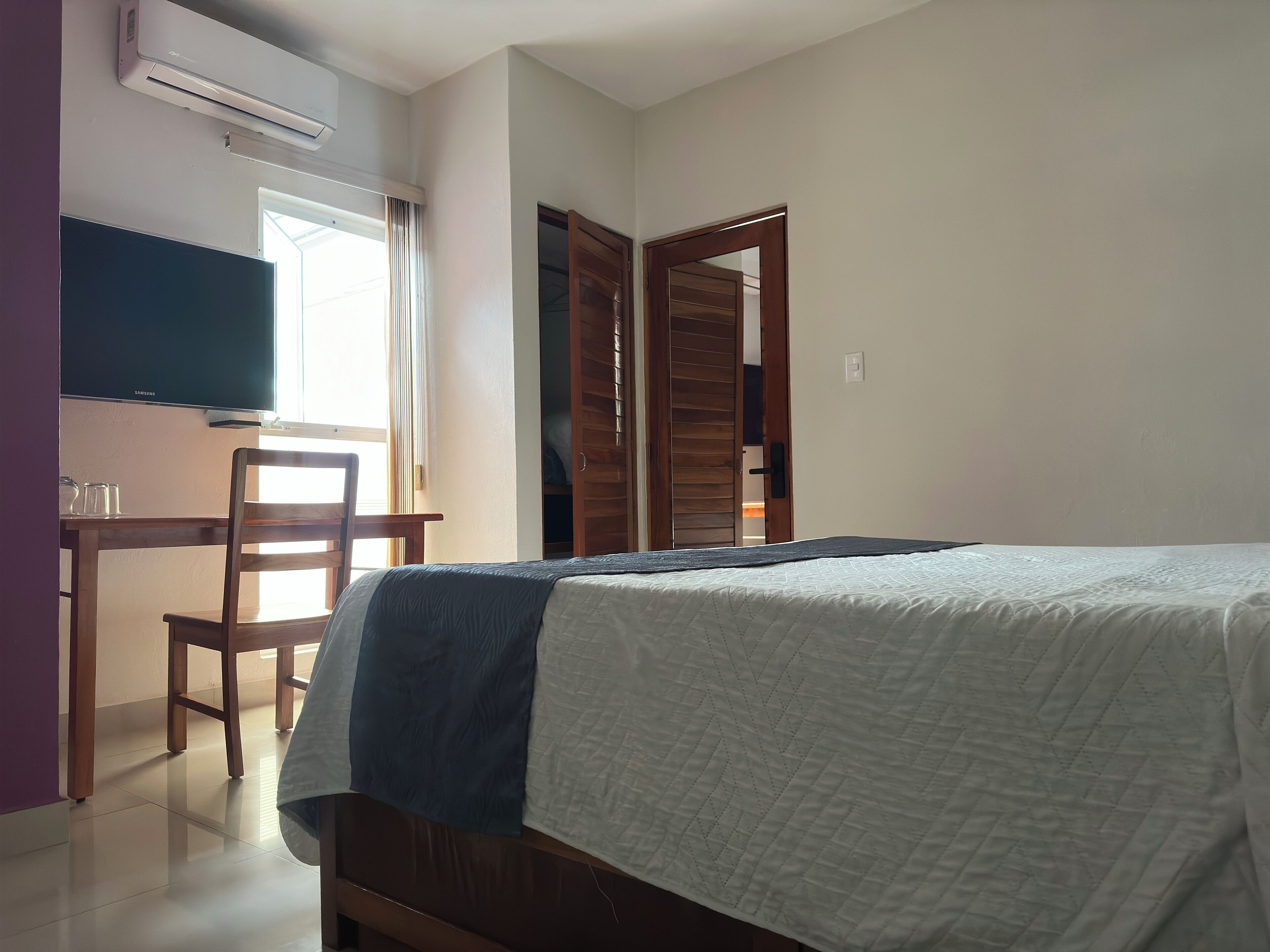 A bedroom with a bed, a desk with a chair, a TV, and a wardrobe.