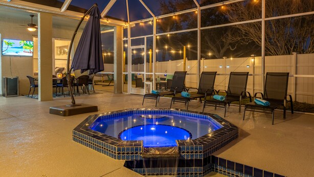 Un espacio al aire libre cubierto con un jacuzzi, sillas y luces colgantes.