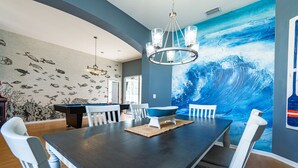 Un comedor con una mesa de madera oscura, sillas blancas, un tazón azul y un mural de peces y una ola.