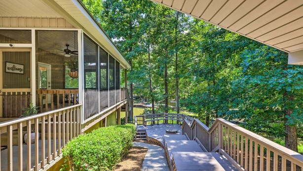 A covered outdoor deck with a wooden railing, a "Welcome" sign, and a view of a forested area. - Waterfront Eatonton Escape w/ Private Hot Tub! (Eatonton)