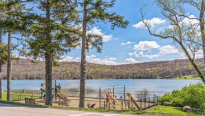 Un parque con juegos infantiles, un lago y una colina boscosa al fondo.