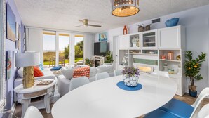Una sala de estar moderna con una mesa de comedor blanca, sofás blancos y un ventilador de techo.