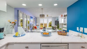 Una cocina moderna con encimeras de mármol blanco, un comedor con mesa de vidrio y vistas al exterior.