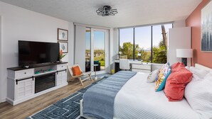 Un dormitorio moderno con una cama grande, televisor, escritorio y balcón con vistas.