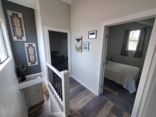 Un escalier menant à une chambre à coucher comprenant un lit, un petit coin salon et une porte donnant sur une autre pièce.