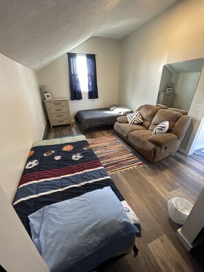 Une petite pièce bien éclairée, avec un lit, un canapé, une table de chevet et une fenêtre avec des rideaux.