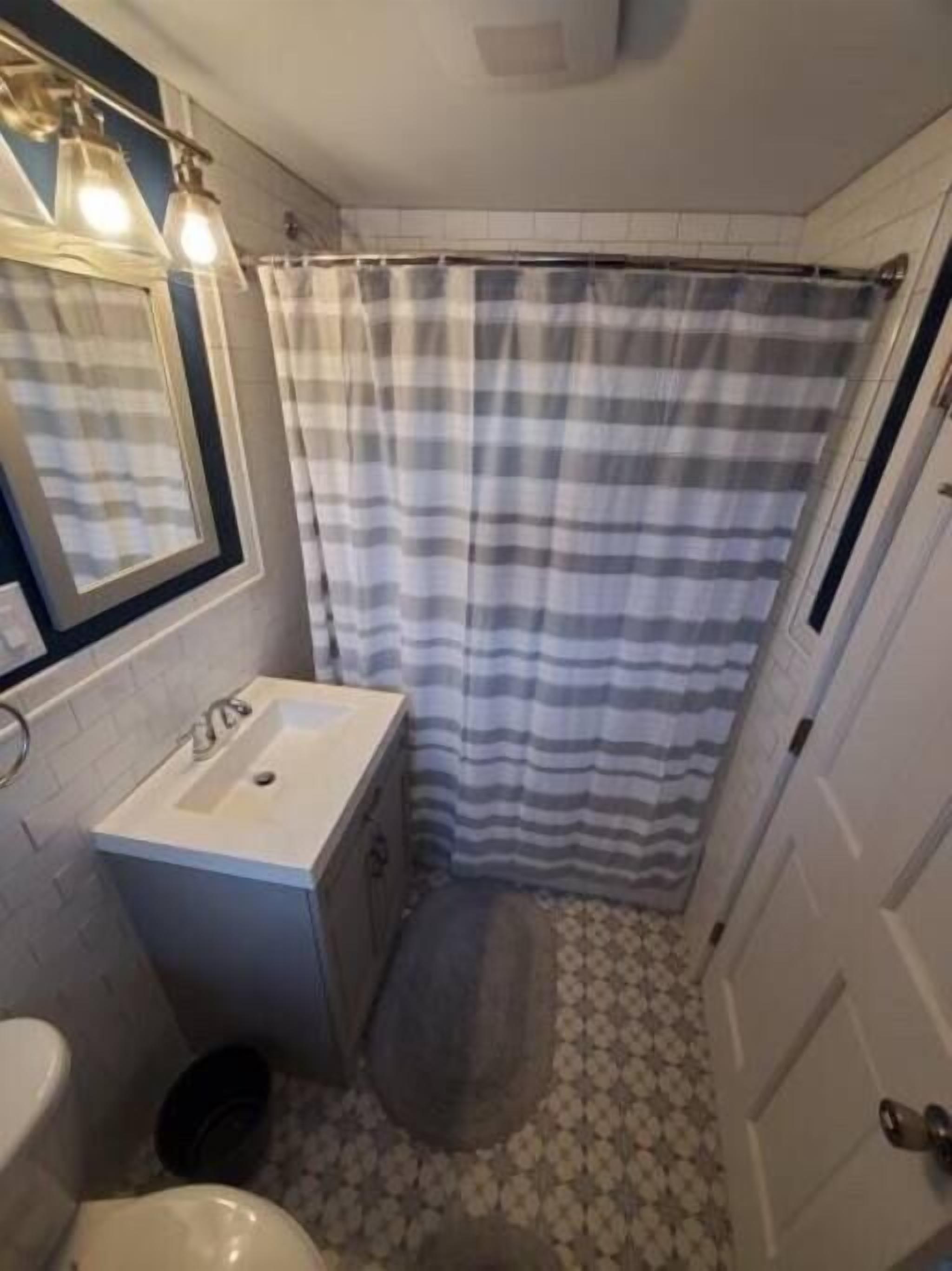 A bathroom with a white sink, a mirror, a striped shower curtain, and a patterned floor.