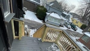 Une terrasse en bois recouverte de neige, avec une rambarde en bois et un paillasson.