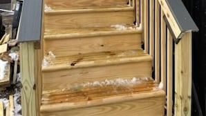 Un escalier en bois, doté d’une rampe métallique, mène à un bâtiment sombre également en bois.