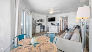 A compact living space with a kitchenette, a dining area with woven tables, and a sofa. - 🚤Belleair Beach Club #313 – Cozy Gulf-Front Condo with Stunning Views & Heated Pool!🩱 (Belleair Beach)