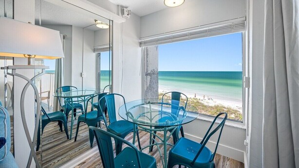 A room with a glass table and chairs, a view of the beach, and a ceiling light. - 🚤Belleair Beach Club #313 – Cozy Gulf-Front Condo with Stunning Views & Heated Pool!🩱 (Belleair Beach)