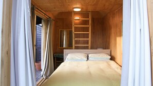 A wooden room with a bed, a ladder, and a window.