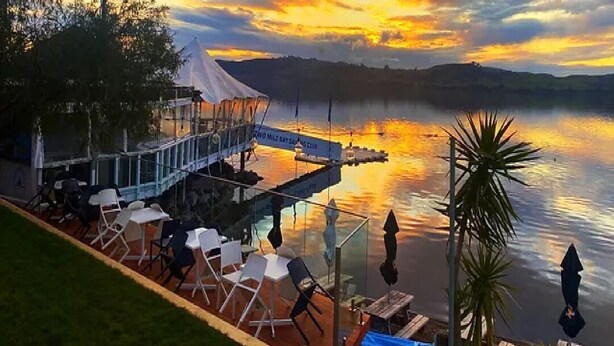 A lakeside dining area with outdoor seating and a view of the sunset.