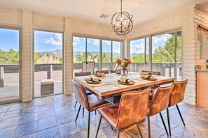 A spacious dining area with a large table set for six, surrounded by leather chairs, large windows offering a mountain view, and a modern chandelier. - Patio & Panoramic Desert Views: Sedona Getaway! (Sedona)