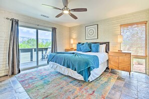 A bedroom with a bed, a ceiling fan, a nightstand, a lamp, a window with blinds, and a view of the outdoors. - Patio & Panoramic Desert Views: Sedona Getaway! (Sedona)