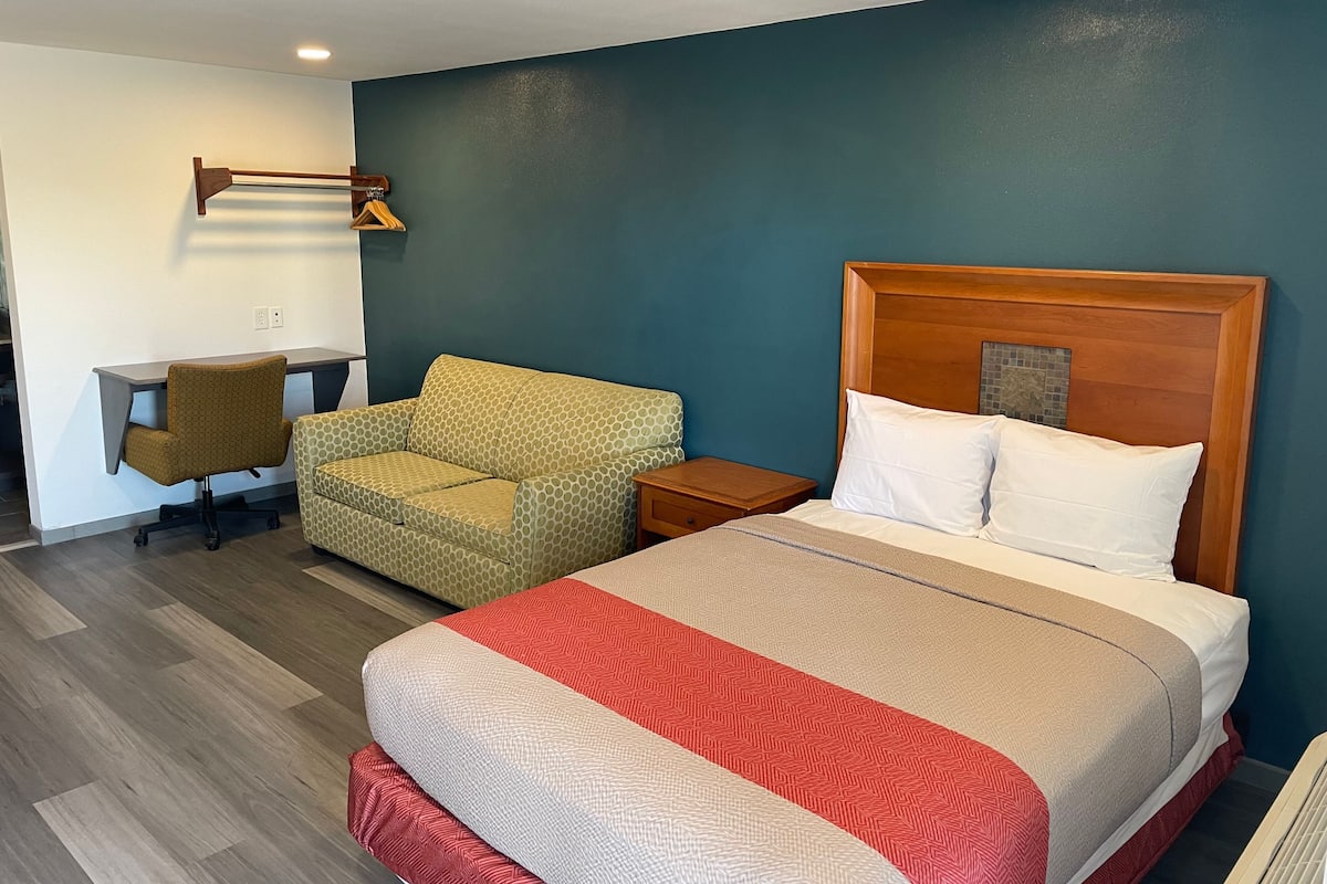 A hotel room with a bed, a desk, a chair, and a nightstand.