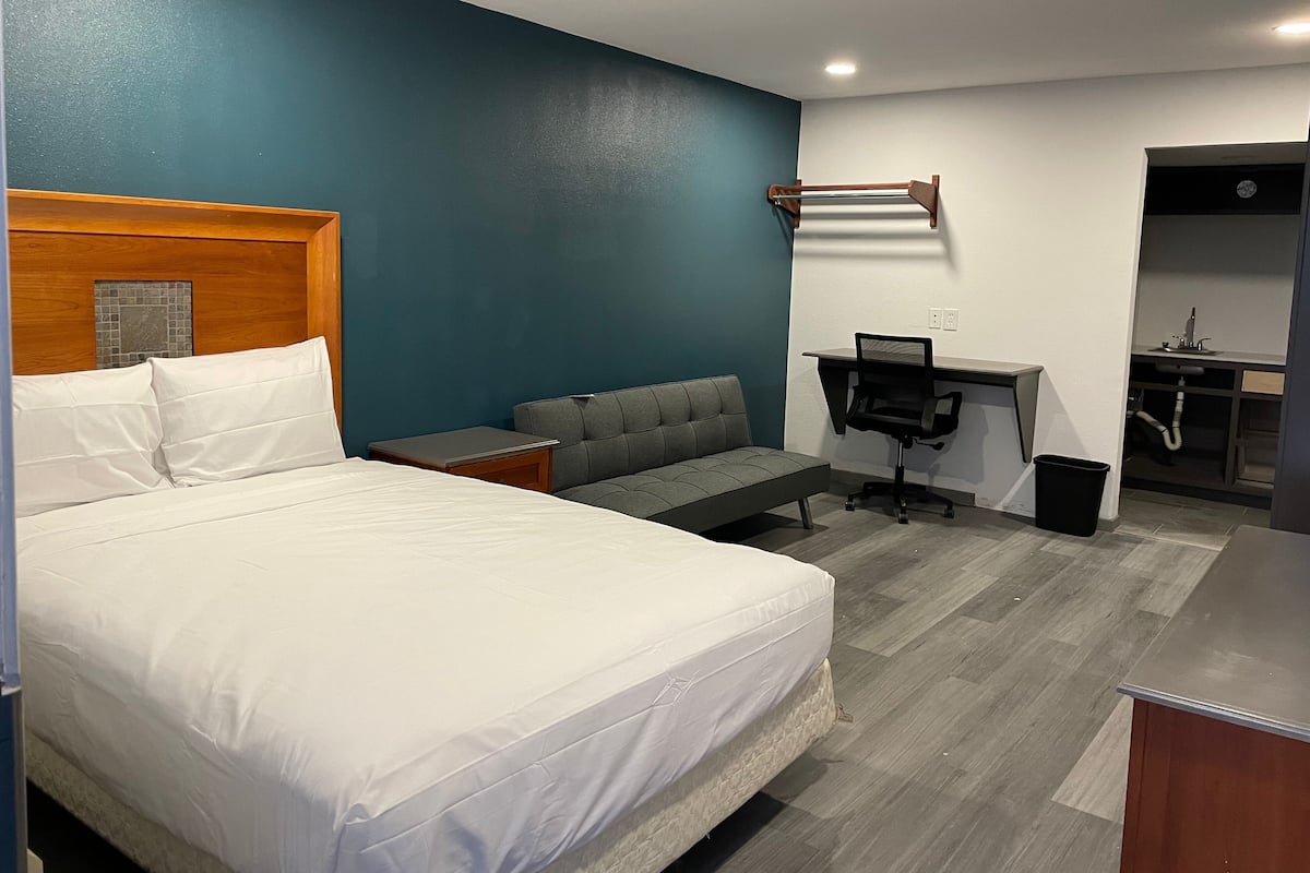 A hotel room with a bed, a sofa, a desk with a chair, and a small kitchenette.