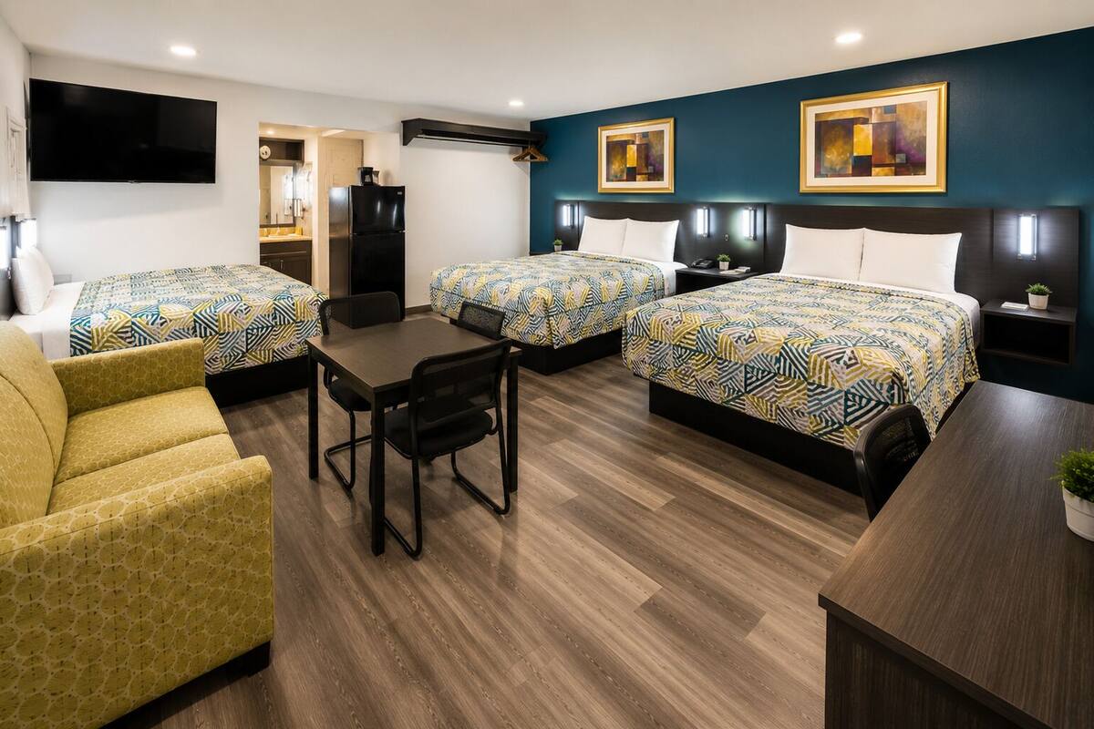 A hotel room with two beds, a desk, a chair, a TV, and artwork on the walls.