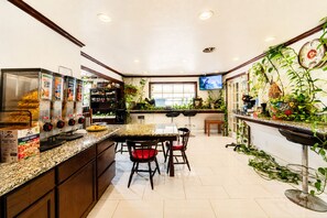 A kitchen with a granite countertop, wooden cabinets, a dining area with chairs, and a television mounted on the wall.