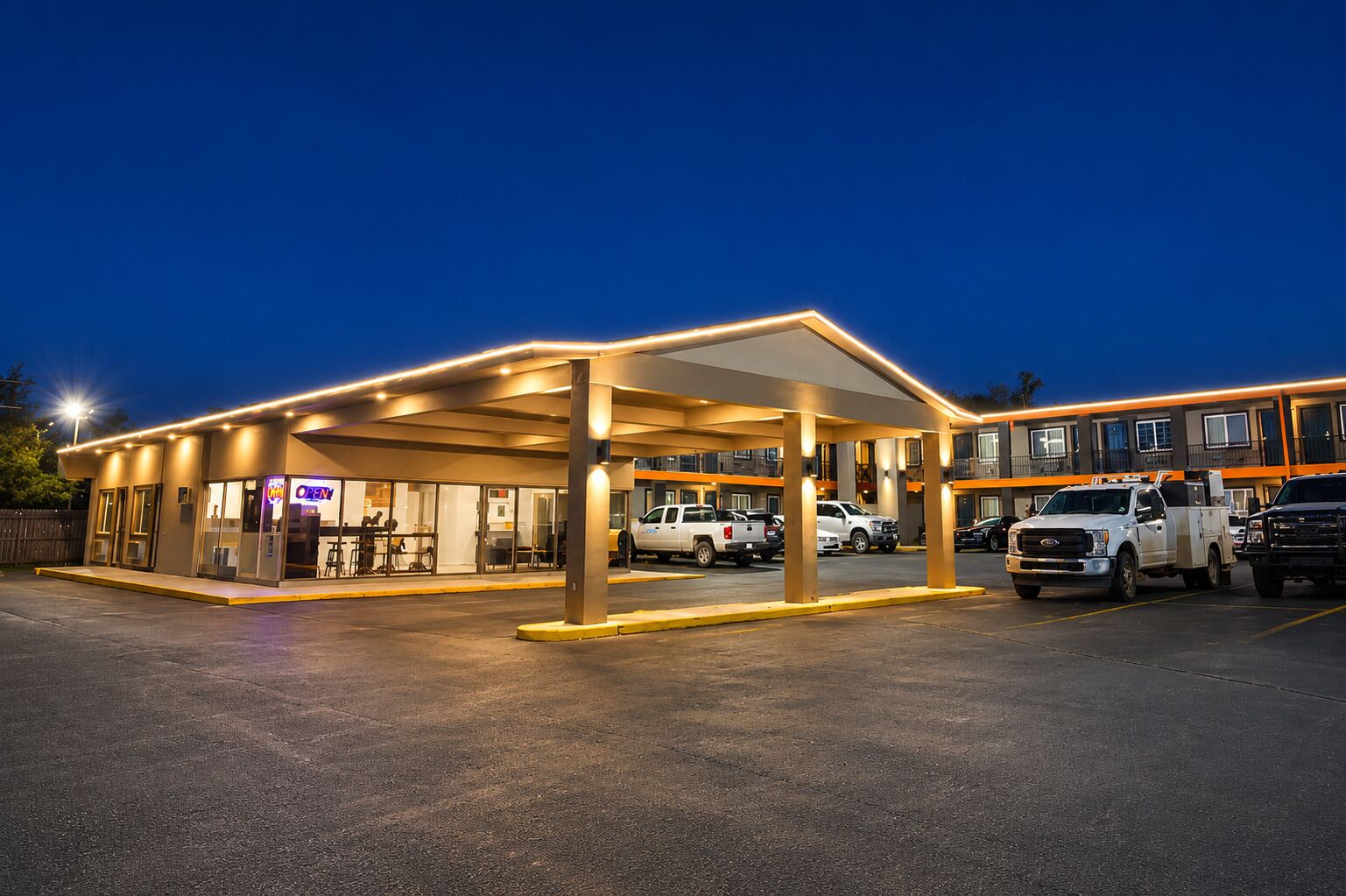 Ett hotell med ett takförsett parkeringsområde, flera fordon och en väl synlig restaurangskylt.